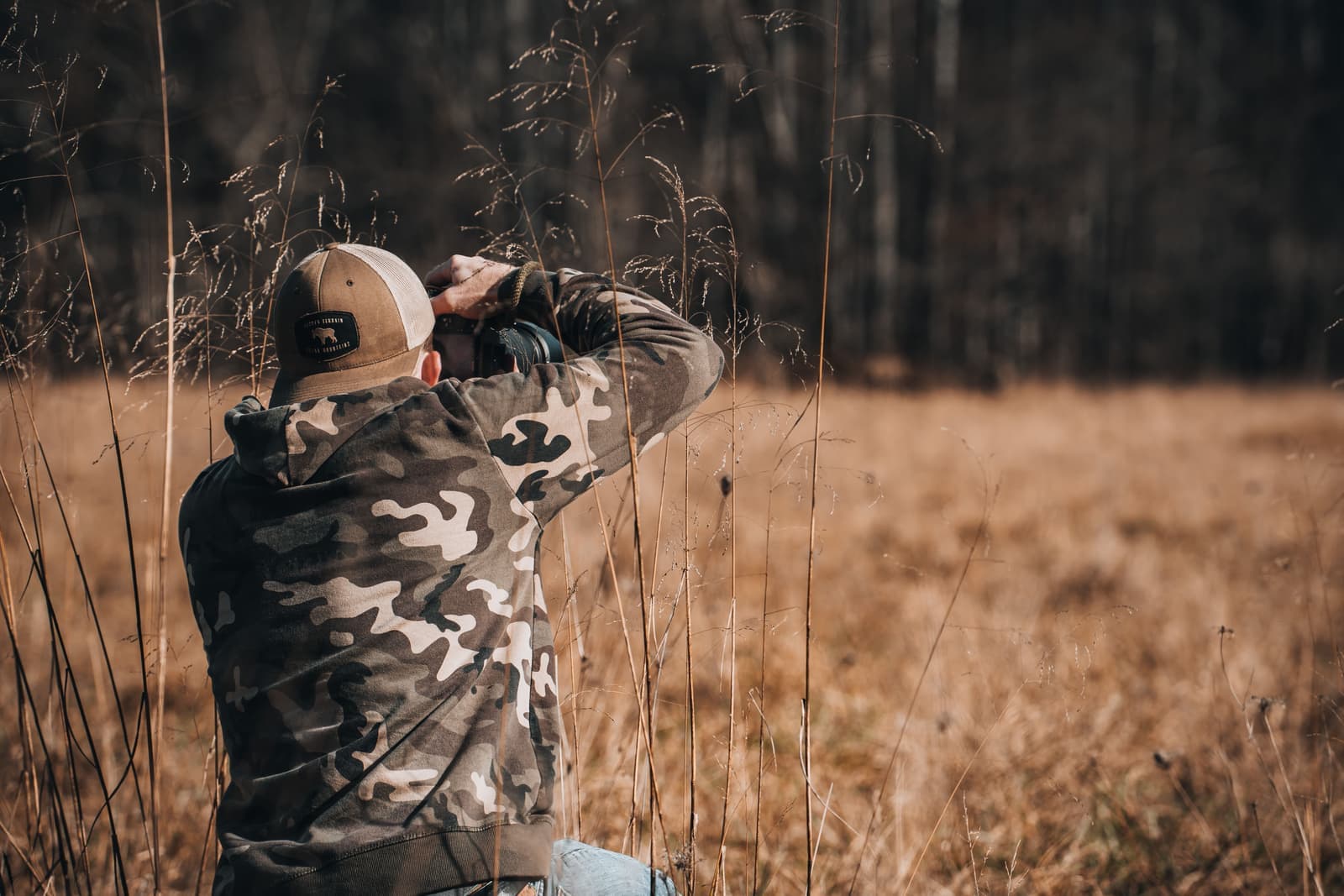 A person in camouflage photographing wildlife from a grassy field